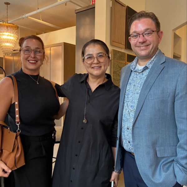 Three men in matching vests posing in front of a red brick building and a garden with tulips.